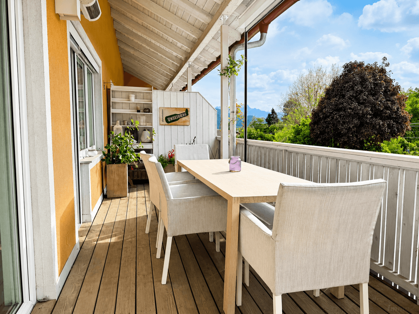 Geräumiger Balkon mit Holzboden und Essbereich, umgeben von viel Grün.