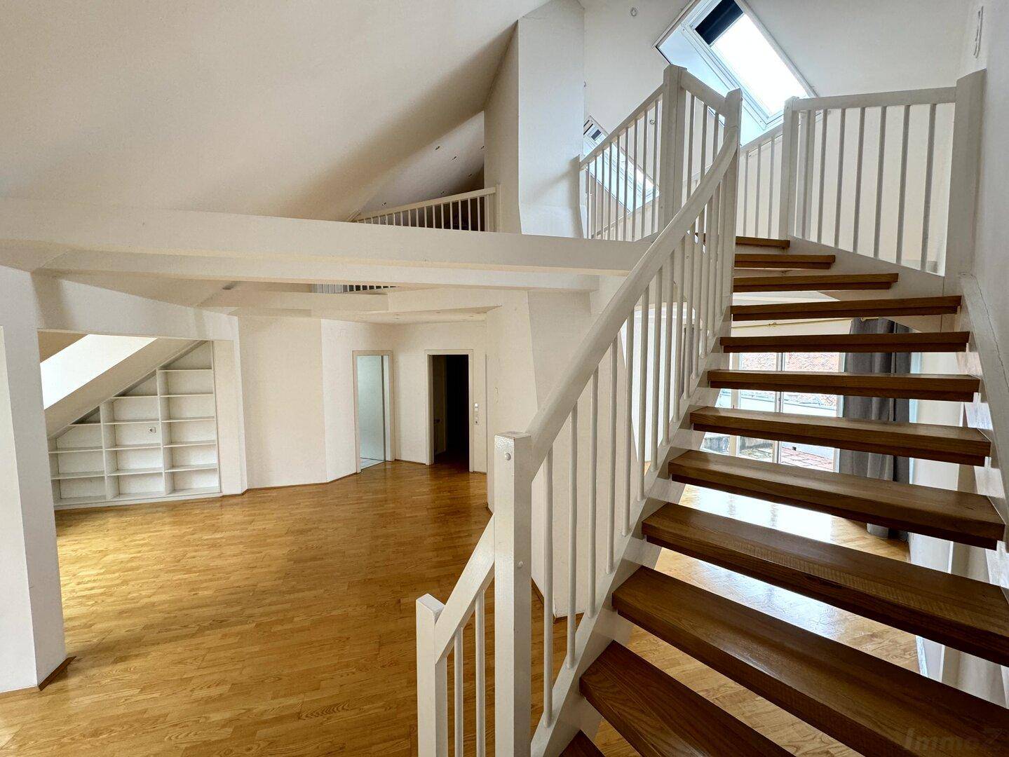 Heller Wohnbereich im Dachgeschoss mit Holztreppe, sichtbaren Balken und Dachfenstern für viel Tageslicht.