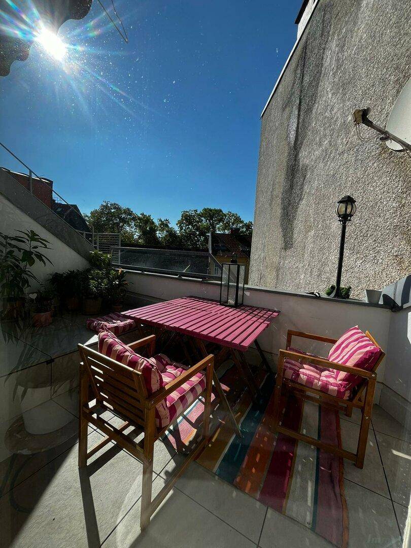 Sonnige Dachterrasse mit farbenfrohen Gartenmöbeln und einem Teppich, ideal zum Entspannen im Freien.