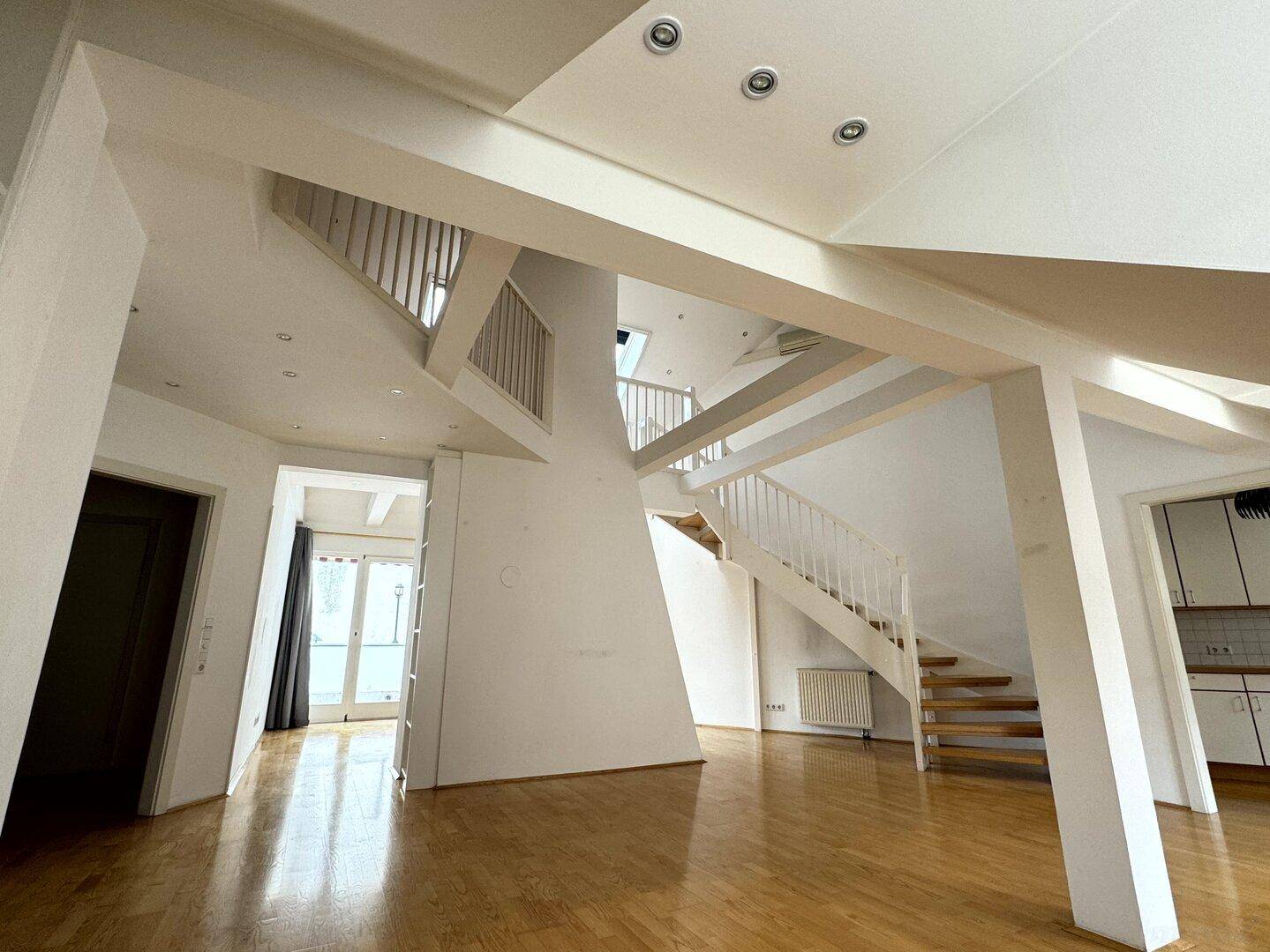 Großzügiger offener Wohnbereich mit Holzboden, sichtbaren Balken, Treppe und integrierter Beleuchtung.