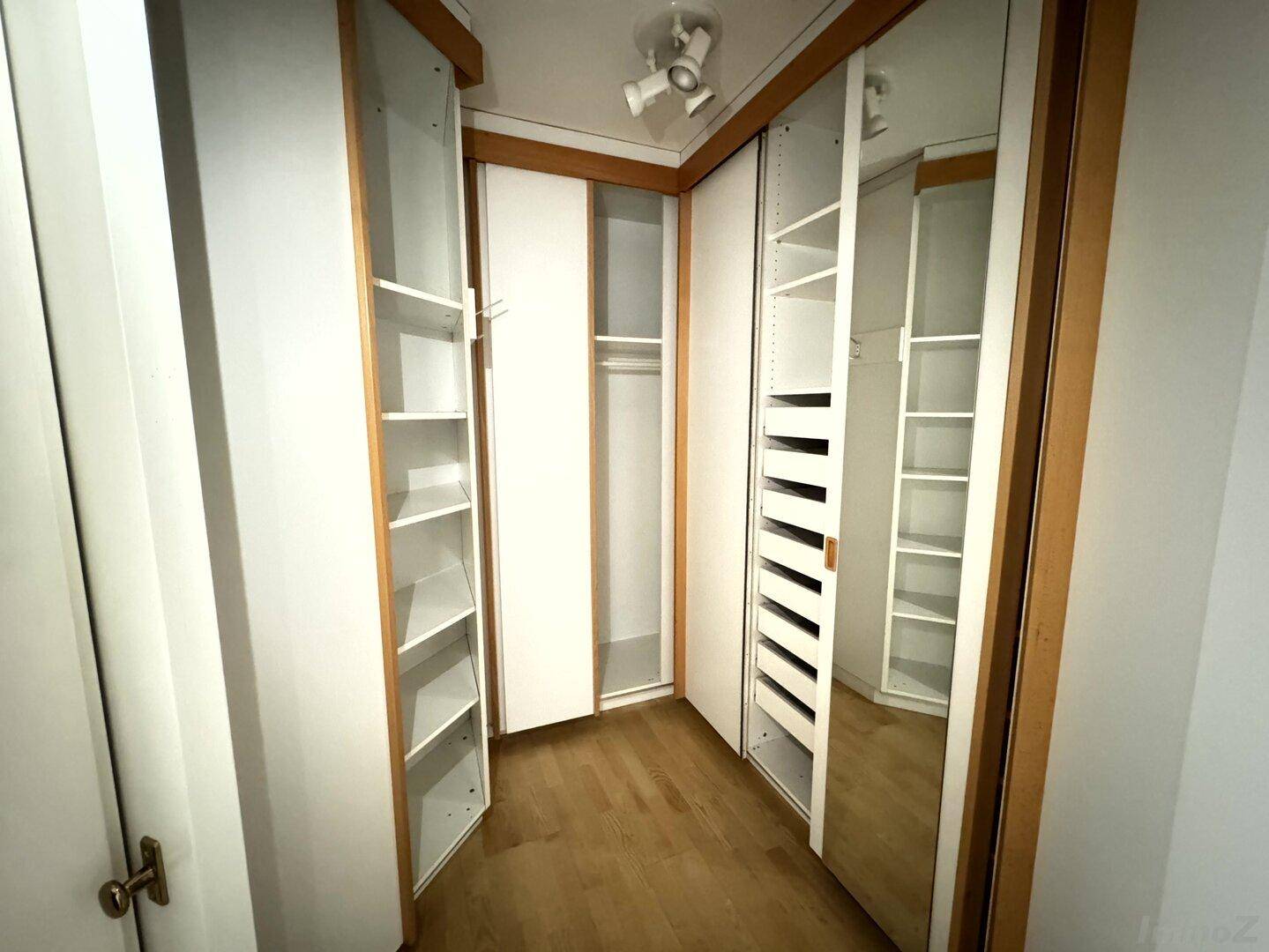 Praktischer begehbarer Kleiderschrank mit integrierten Regalen und Spiegeltüren für viel Stauraum.