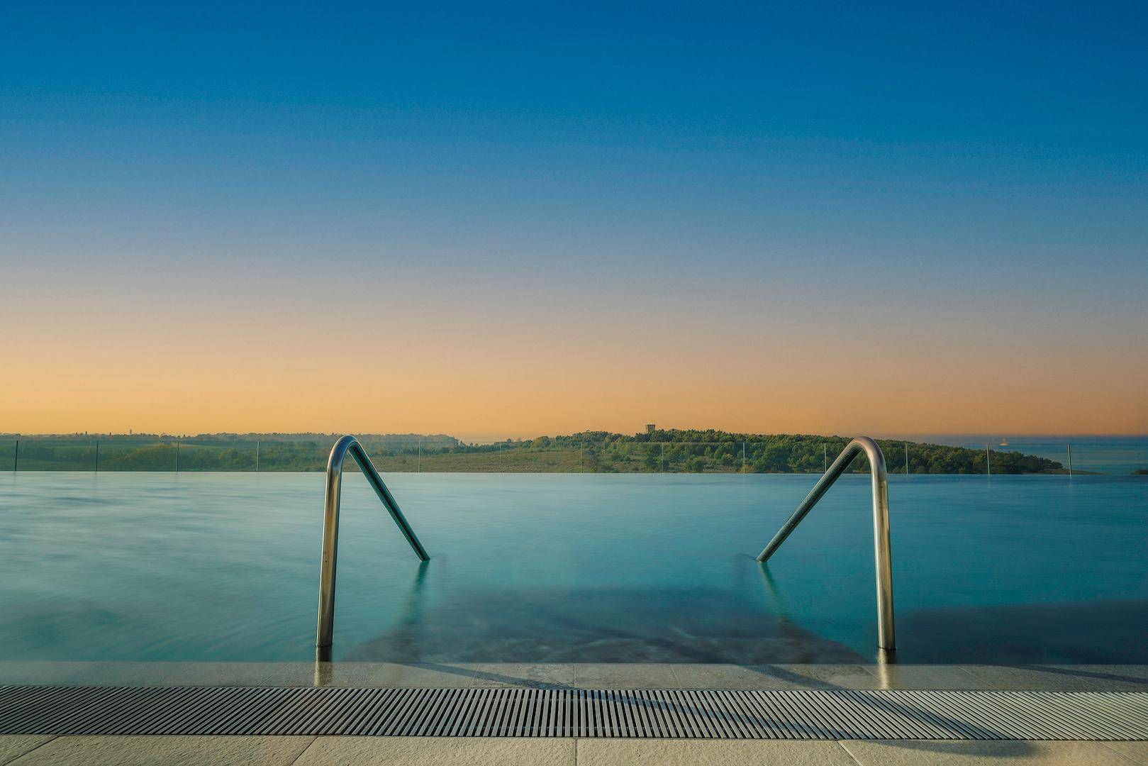 Infinity-Pool mit atemberaubendem Blick auf das Meer und die Küstenlandschaft bei Sonnenuntergang.