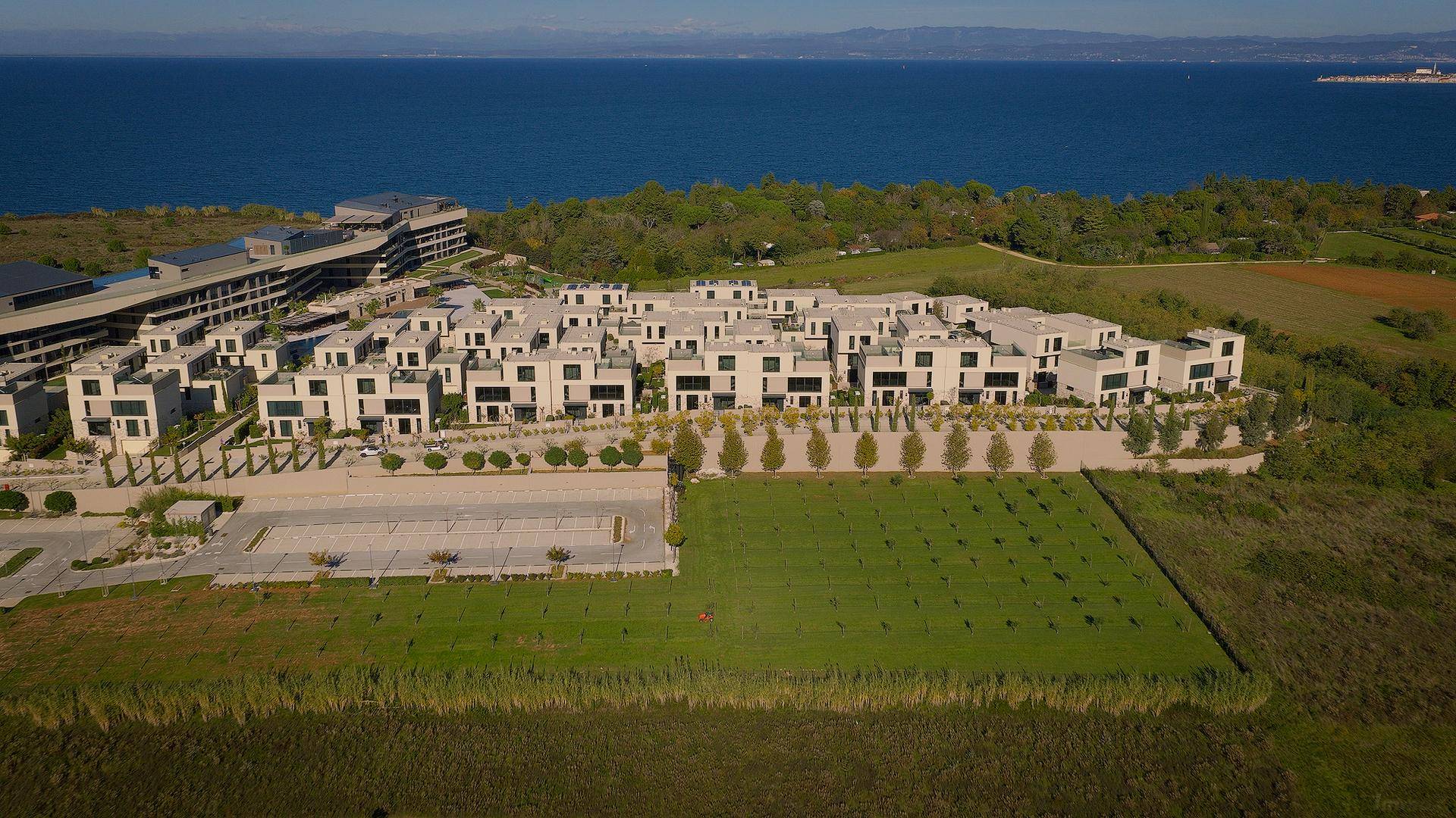 Luftaufnahme einer weitläufigen Wohnanlage mit vielen Häusern direkt am Meer und großen Grünflächen.