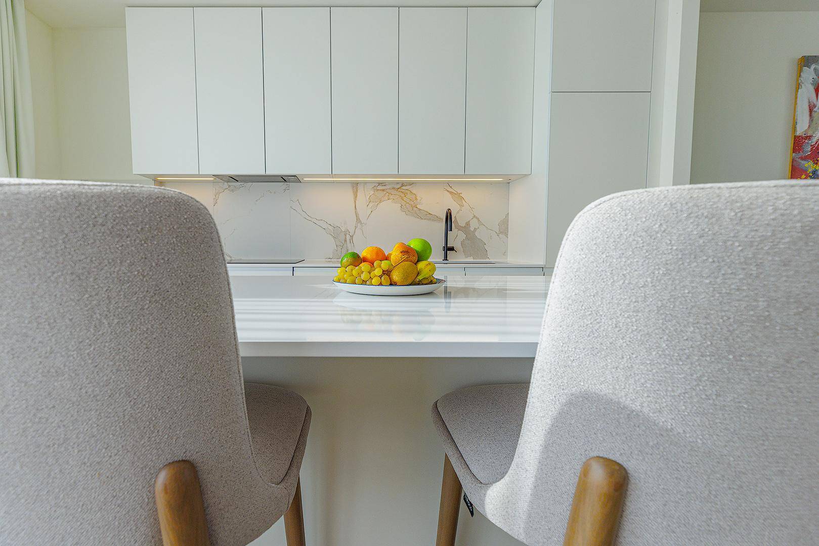 Moderne Küchenzeile mit weißer Arbeitsplatte, Marmorrückwand und frischem Obst.