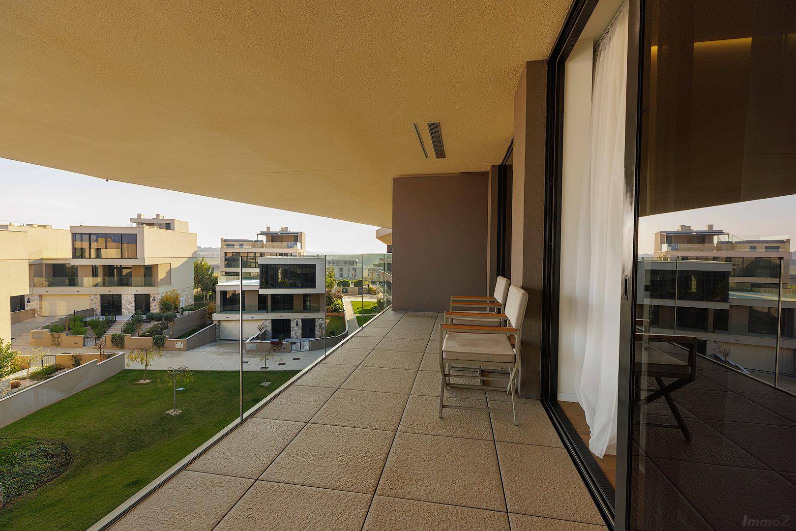 Geräumiger Balkon mit Glasgeländer und Blick auf die umliegenden modernen Gebäude und Grünflächen.