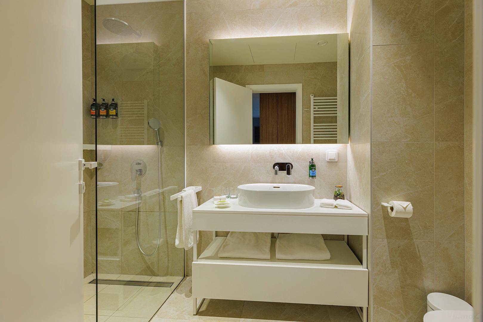 Modernes Badezimmer mit begehbarer Dusche, Einzelwaschbecken und hellen Fliesen.