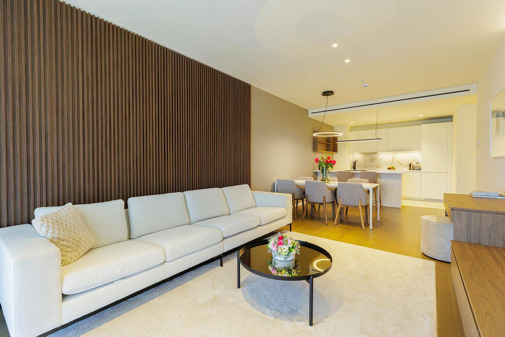 Offener Wohn- und Essbereich mit modernem Sofa, Holzwandverkleidung und integrierter Küche.