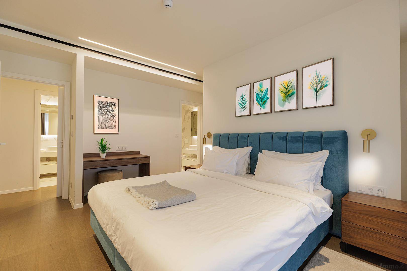 Modernes Schlafzimmer mit großem blauen Bett, Holzelementen und Zugang zum Badezimmer.