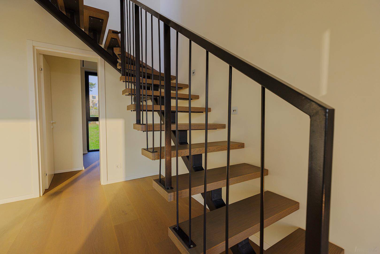 Elegante Holztreppe mit schwarzem Metallgeländer in einem hellen Eingangsbereich.