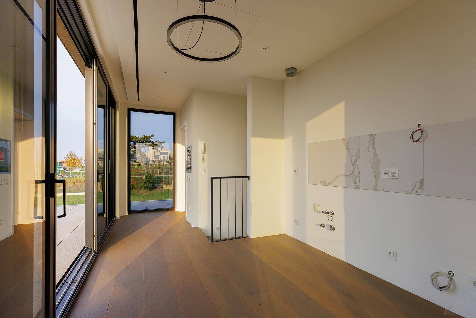 Lichtdurchfluteter Raum mit Holzboden, großen Glasfronten und vorbereiteter Küchenzeile.