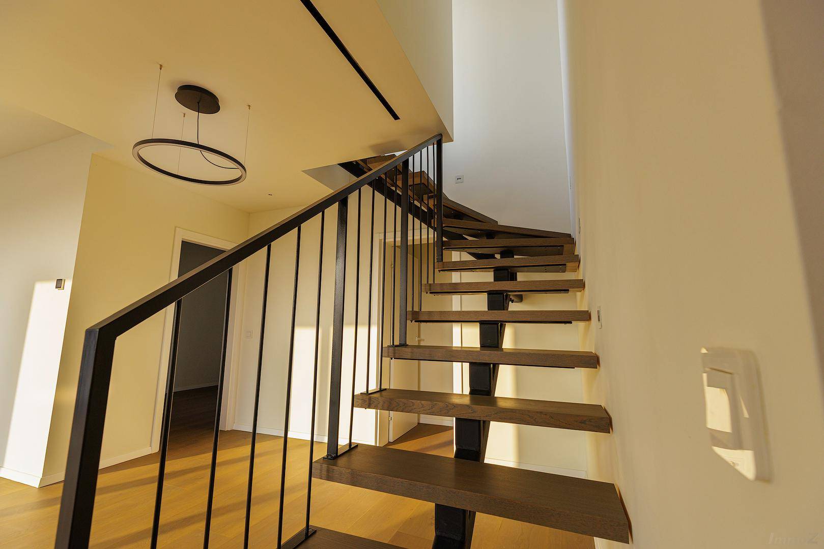 Moderne Holztreppe mit schwarzem Metallgeländer und minimalistischer Deckenbeleuchtung.