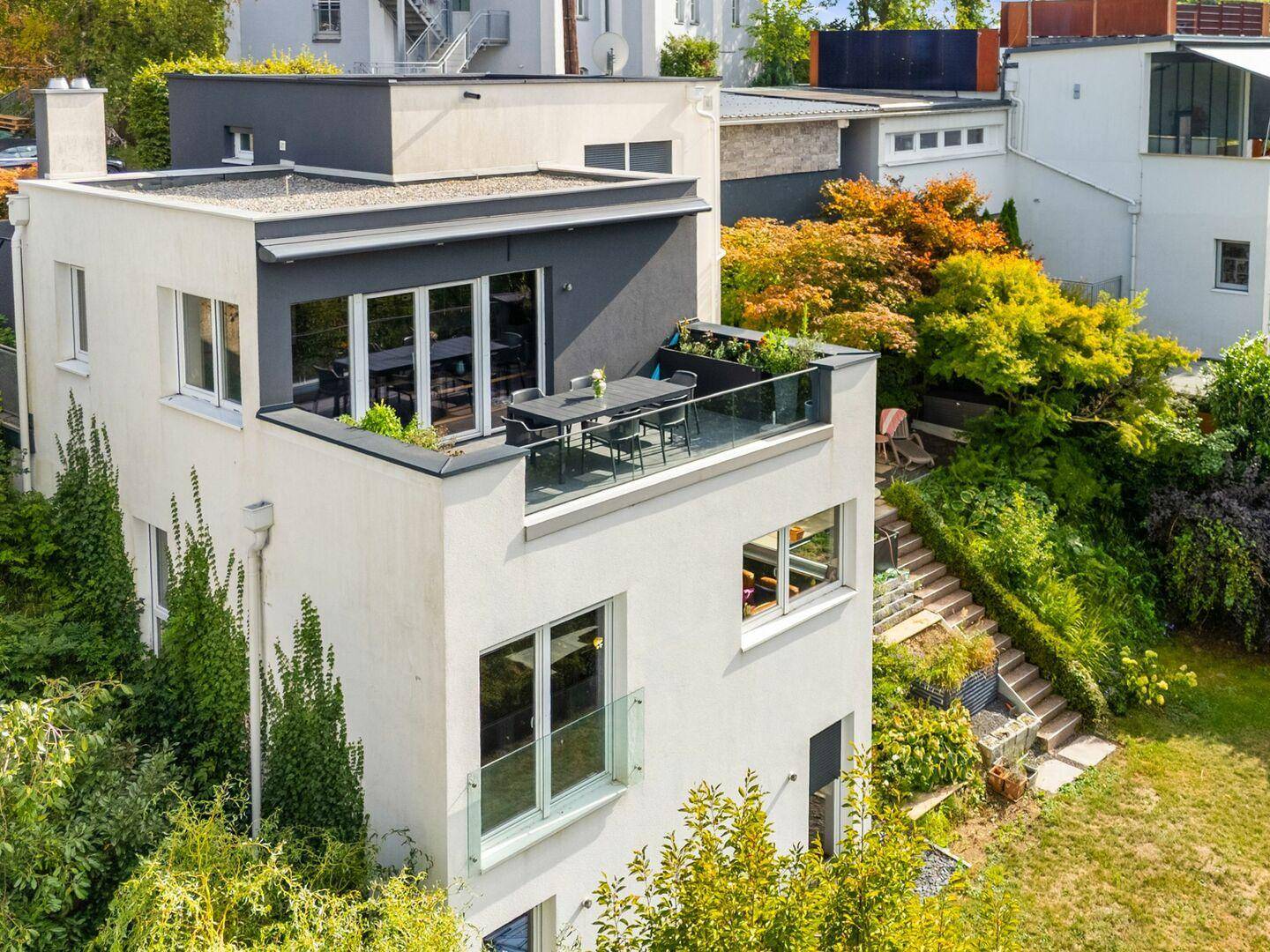Ansicht des modernen Hauses von oben mit Dachterrasse und umliegender grüner Landschaft.