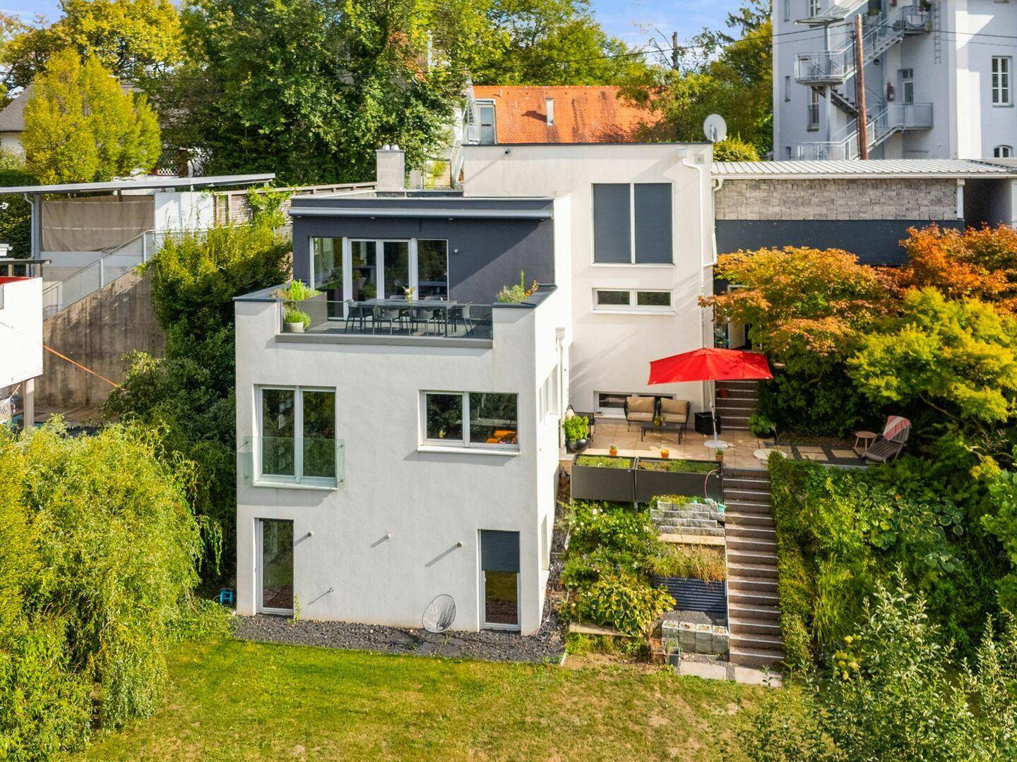 Modernes mehrstöckiges Haus mit Terrassen und Garten in grüner Hanglage.