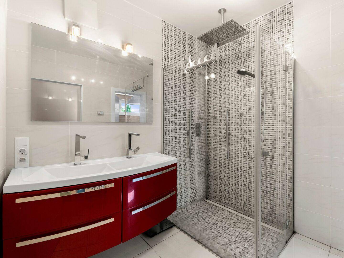 Modernes Badezimmer mit Doppelwaschbecken, roten Unterschränken und begehbarer Regendusche.