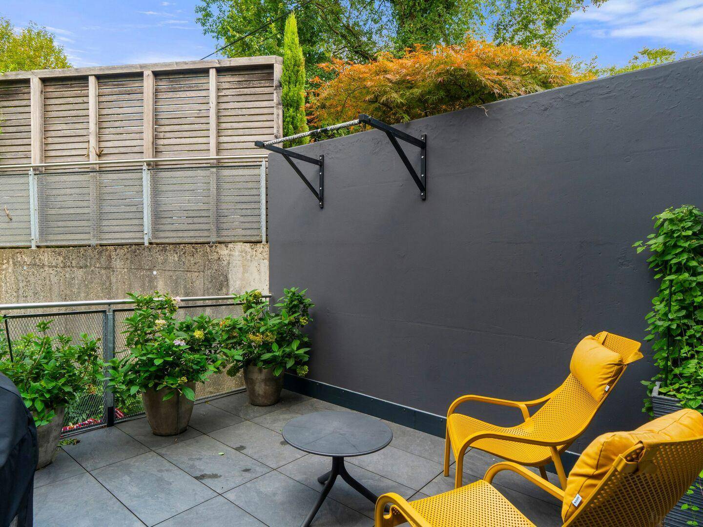 Gemütliche Terrasse mit gelben Liegestühlen, Topfpflanzen und einer Klimmzugstange an der Wand.