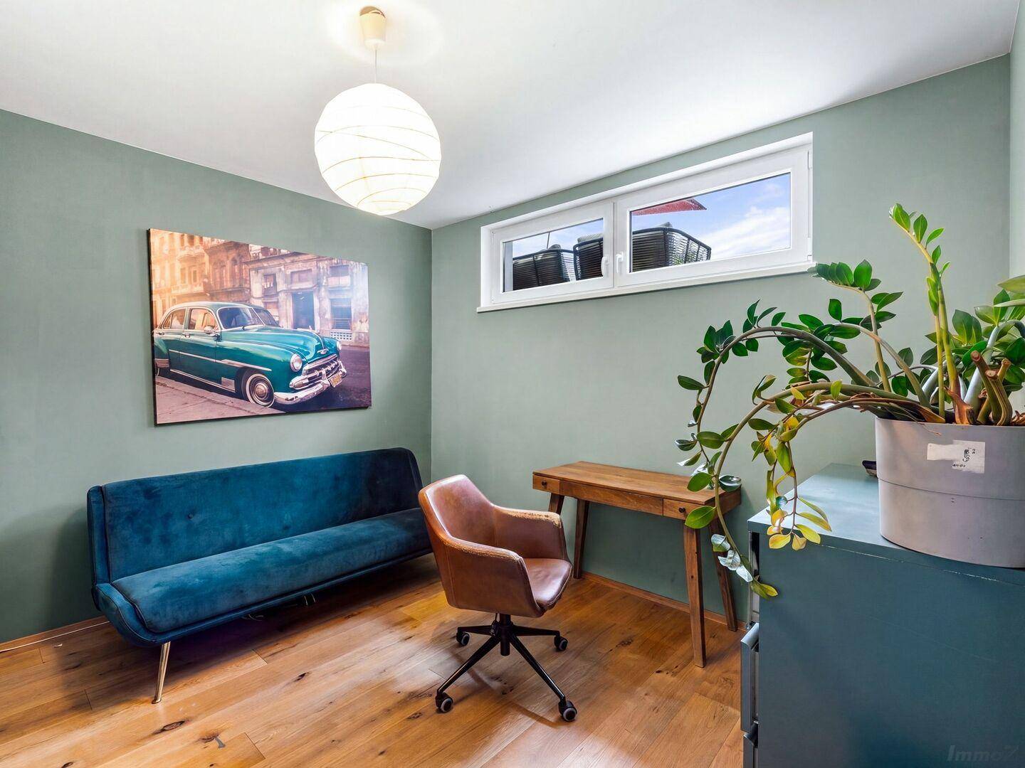 Helles Arbeitszimmer mit blauem Sofa, Holzschreibtisch und grünen Wänden.