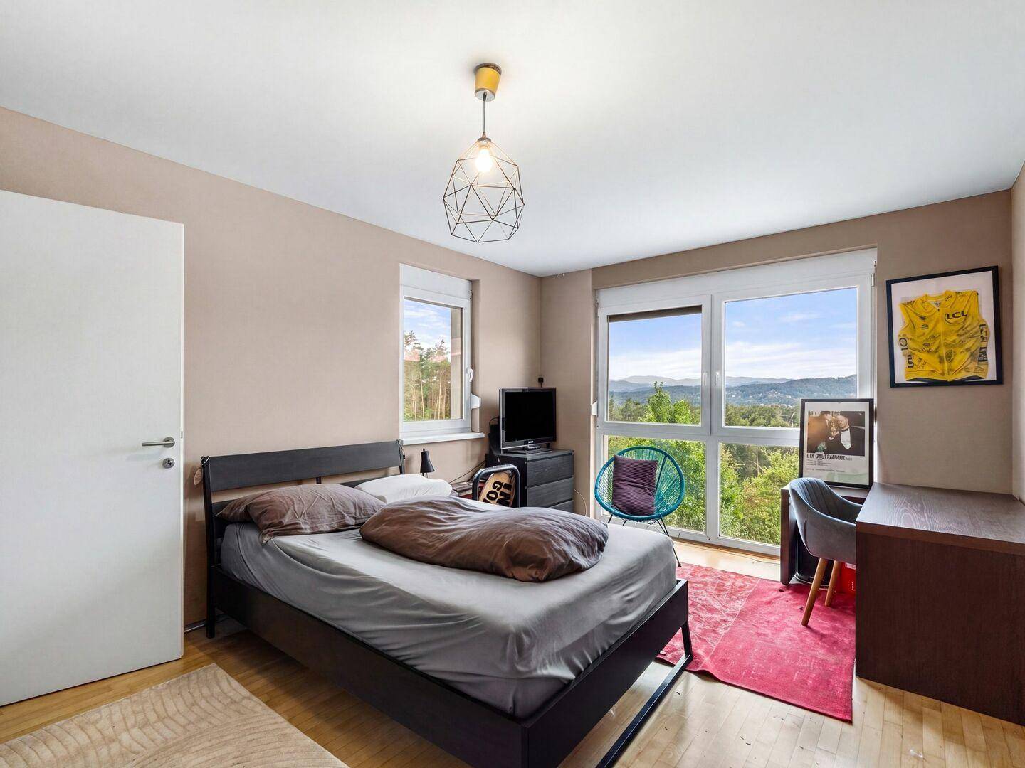Helles Schlafzimmer mit Bett, Schreibtisch und großem Fenster mit Panoramablick.