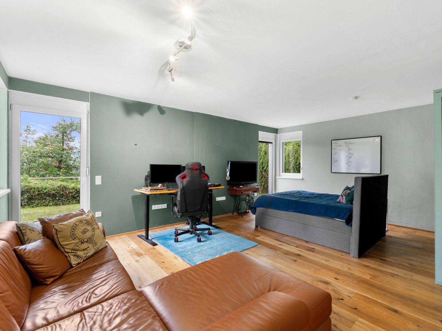 Geräumiges Schlafzimmer mit Bett, Sofa, Arbeitsbereich und Blick ins Grüne.