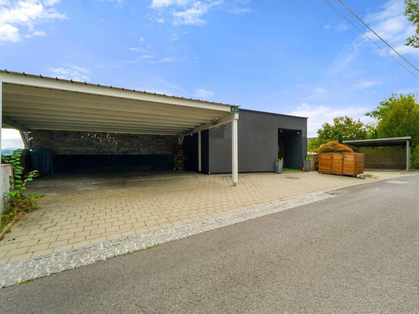 Modernes Gebäude mit großem Carport und gepflasterter Zufahrt in ländlicher Umgebung.