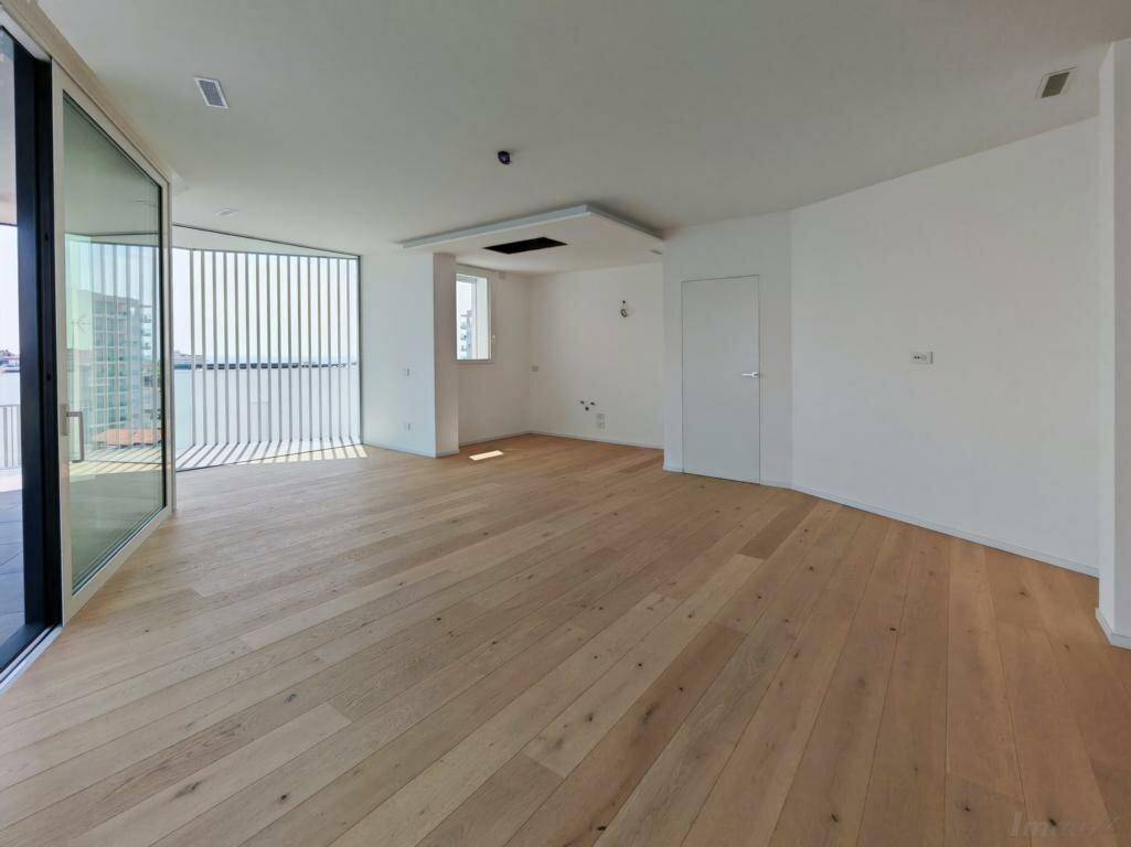 Heller, leerer Wohnraum mit Holzboden und großen Schiebetüren, die zur Terrasse führen.