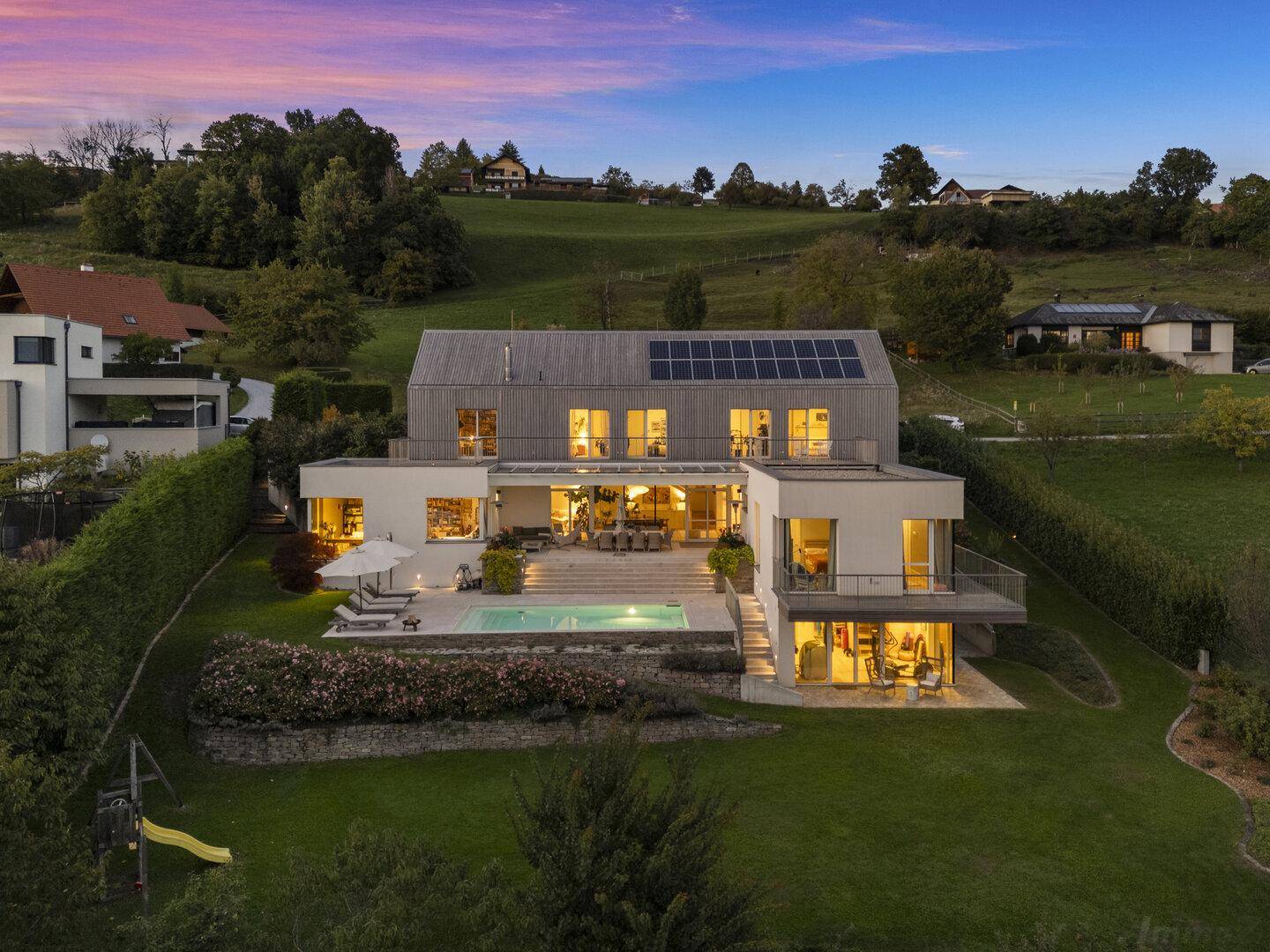 Luxuriöses Anwesen mit modernem Design, großem Pool und weitläufigem Garten bei Sonnenuntergang.