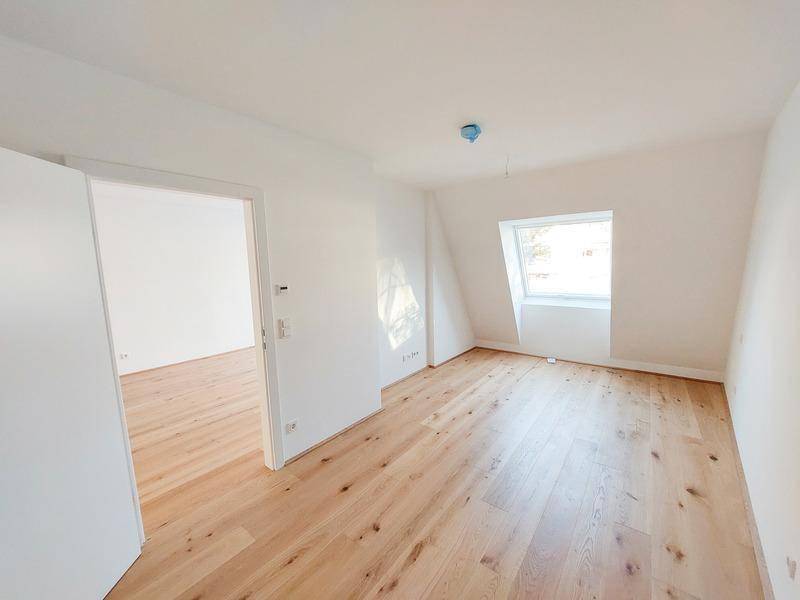 Helles Schlafzimmer mit Holzparkett und einem Fenster in der Dachschräge.