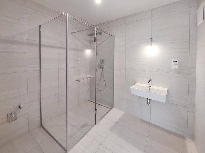 Modernes Badezimmer mit großer Glasdusche, Wandfliesen und minimalistischem Waschbecken.