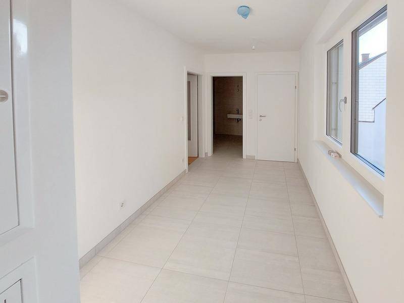 Heller Flur mit hellen Fliesen und Fenstern, die Tageslicht hereinlassen.