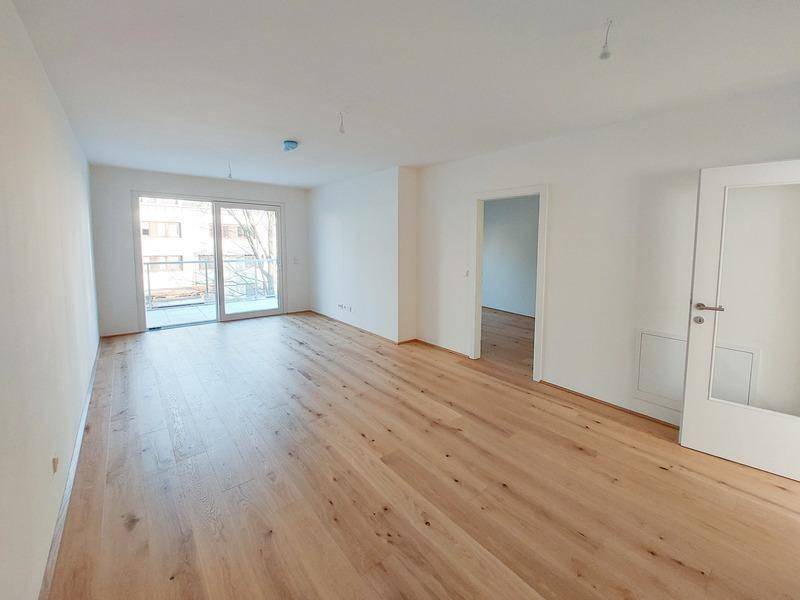 Geräumiges Wohnzimmer mit hellem Holzparkett und Zugang zu einem Balkon.