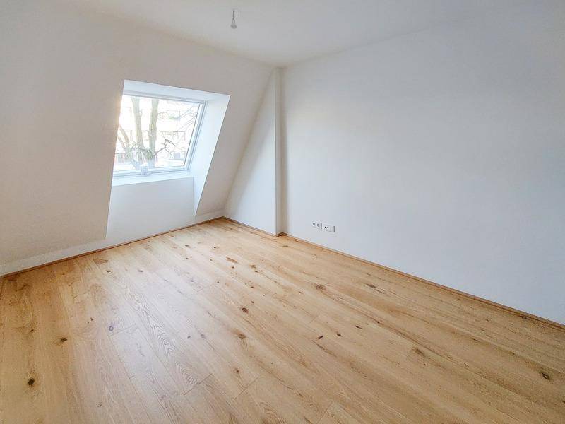 Leeres Zimmer mit Dachschräge, Holzparkett und einem großen Dachfenster für viel Licht.