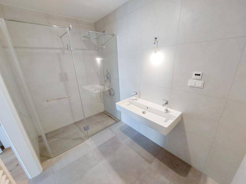 Helles Badezimmer mit begehbarer Dusche, modernem Waschbecken und grauen Wandfliesen.