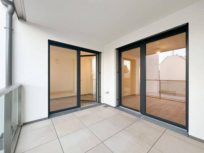 Geräumiger Balkon mit Fliesenboden und Glasgeländer, zugänglich durch große Schiebetüren.