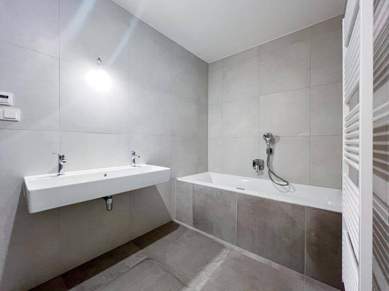 Modernes Badezimmer mit Badewanne, Doppelwaschbecken und grauen Fliesen.