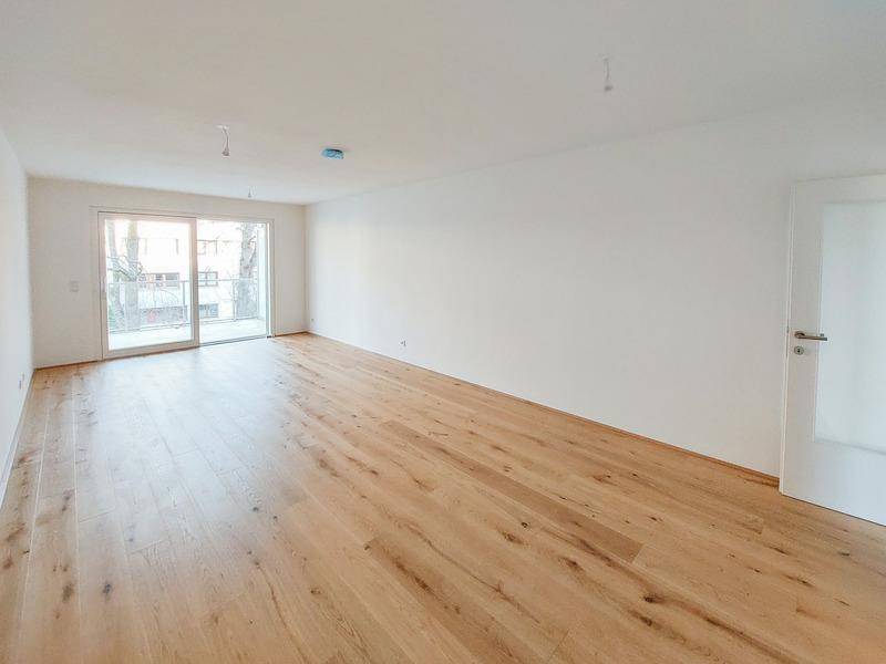 Heller, leerer Wohnbereich mit modernem Holzparkett und Zugang zum Balkon.