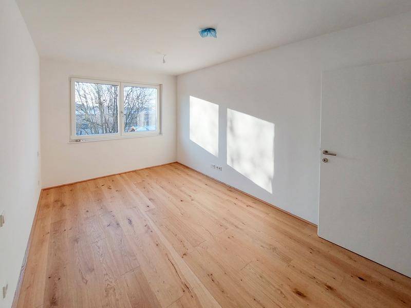 Helles Zimmer mit neuem Holzparkettboden und viel Tageslicht durch das Fenster.