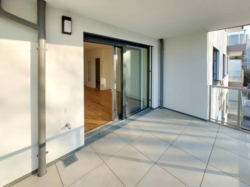 Sonniger Balkon mit Fliesenboden und Glasgeländer, direkt zugänglich vom Innenbereich.