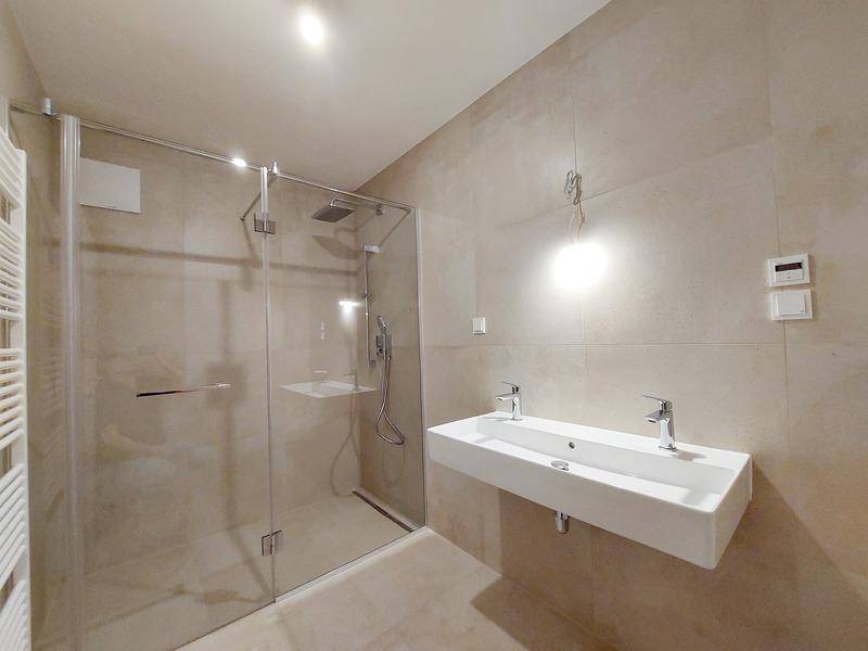 Modernes Badezimmer mit begehbarer Dusche, Doppelwaschbecken und hellen Fliesen.