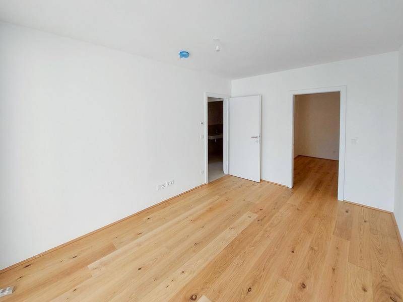 Leeres Zimmer mit hellem Holzboden und zwei Türen, die zu weiteren Räumen führen.