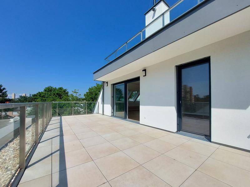 Geräumige Dachterrasse mit Fliesenboden und Glasgeländer unter blauem Himmel.