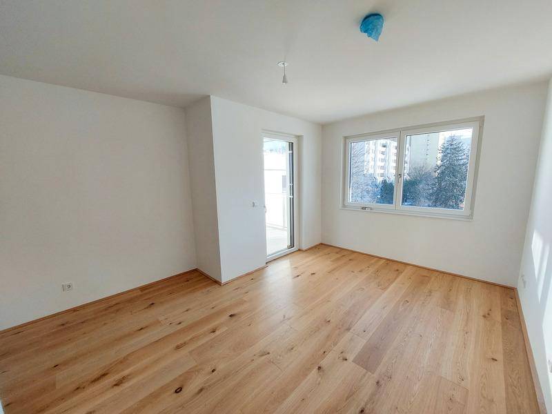 Helles, leeres Zimmer mit Holzboden und Zugang zu einem Balkon oder einer Terrasse.