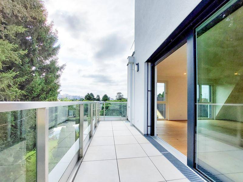 Langer Balkon mit Glasgeländer und Fliesenboden, bietet einen weiten Blick ins Grüne.