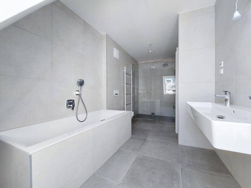 Modernes Badezimmer mit hellgrauen Fliesen, Badewanne, begehbarer Dusche und beheiztem Handtuchhalter.