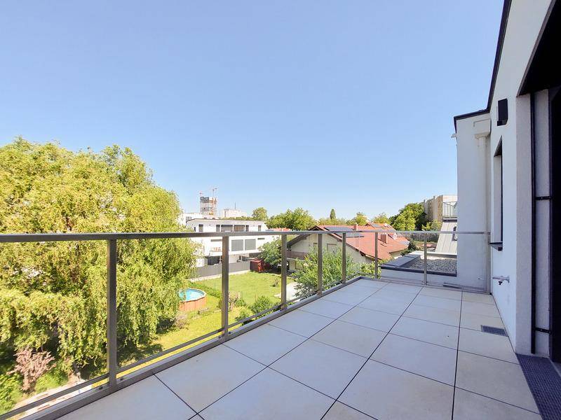 Geräumiger Balkon mit Fliesenboden und Glasgeländer, bietet einen weiten Blick ins Grüne.