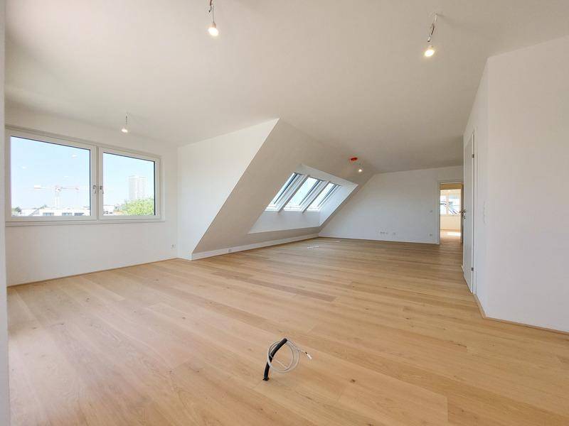 Lichtdurchfluteter Wohnraum mit Holzboden, breiten Fenstern und zusätzlichen Dachfenstern.