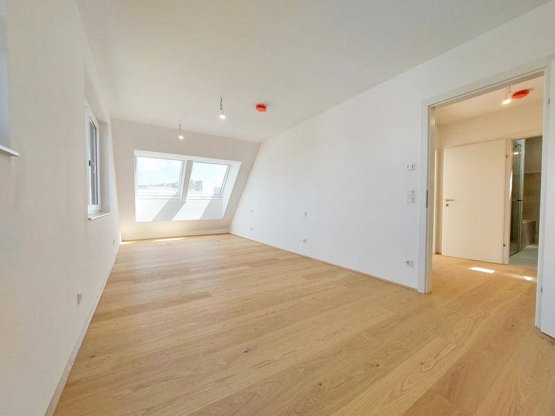 Helles Schlafzimmer mit Holzboden, Dachfenstern und Zugang zu einem modernen Badezimmer.