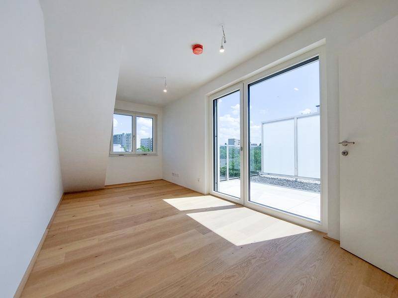 Geräumiges Zimmer mit Holzboden und großem Schiebefenster zum Zugang einer Terrasse.