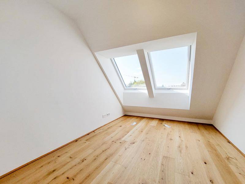 Helles Schlafzimmer im Dachgeschoss mit Holzboden und zwei großen Dachfenstern.