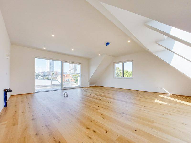 Helles Dachgeschosszimmer mit Holzboden, großen Fenstern und Zugang zu einem Balkon.