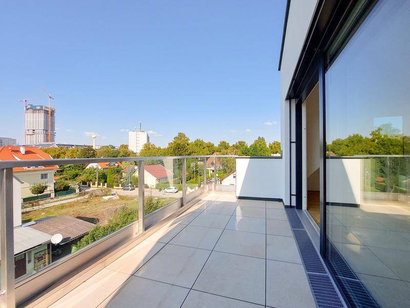 Großer Balkon mit Fliesenboden, Glasgeländer und Blick auf die Stadt.