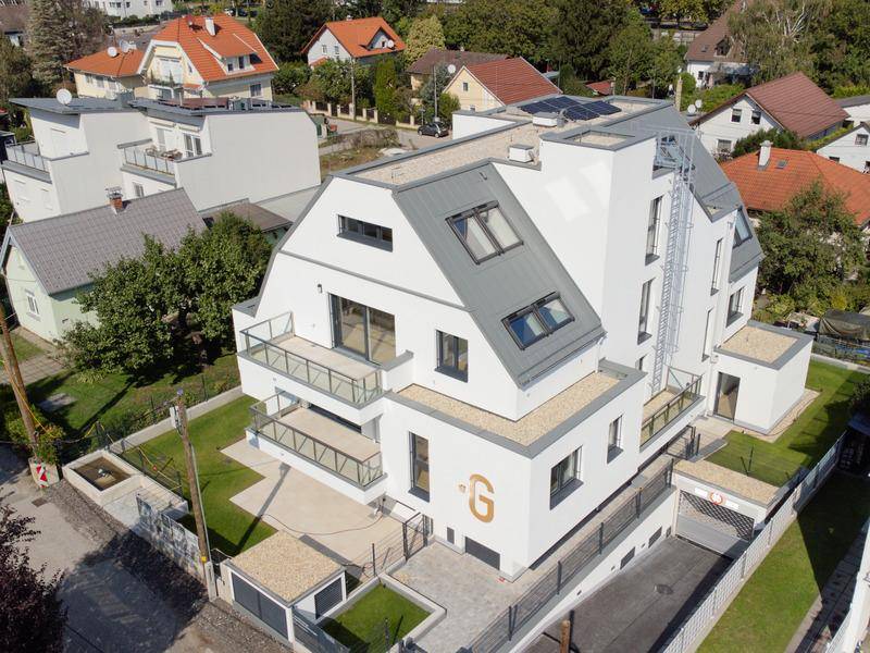 Moderne Wohnanlage mit mehreren Balkonen, Dachschrägen und Photovoltaikanlage auf dem Dach.